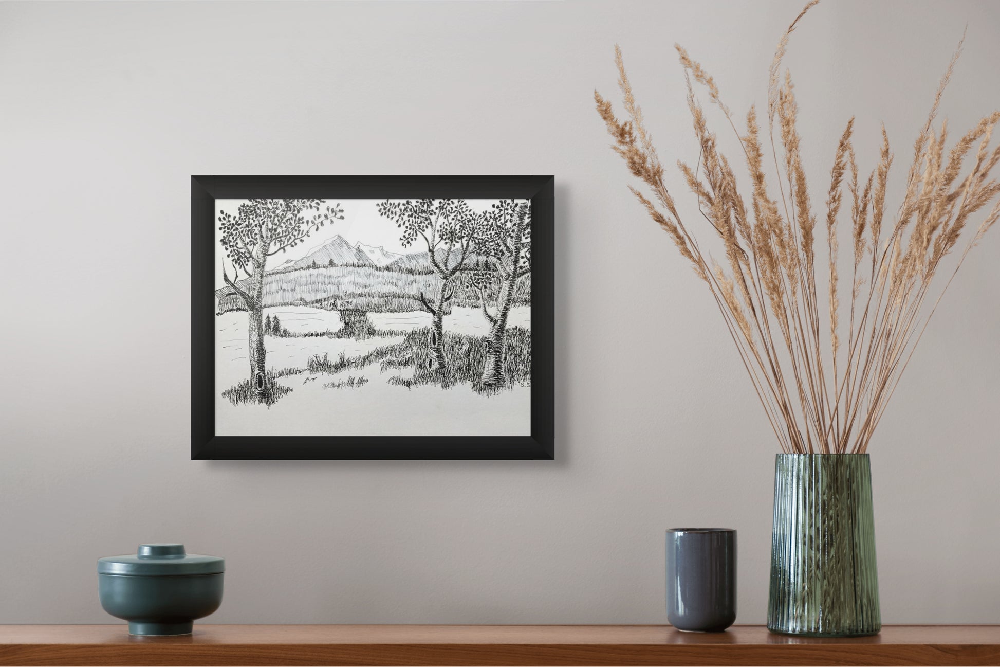 Framed black and white landscape print on a wall above a wooden shelf with decorative items.