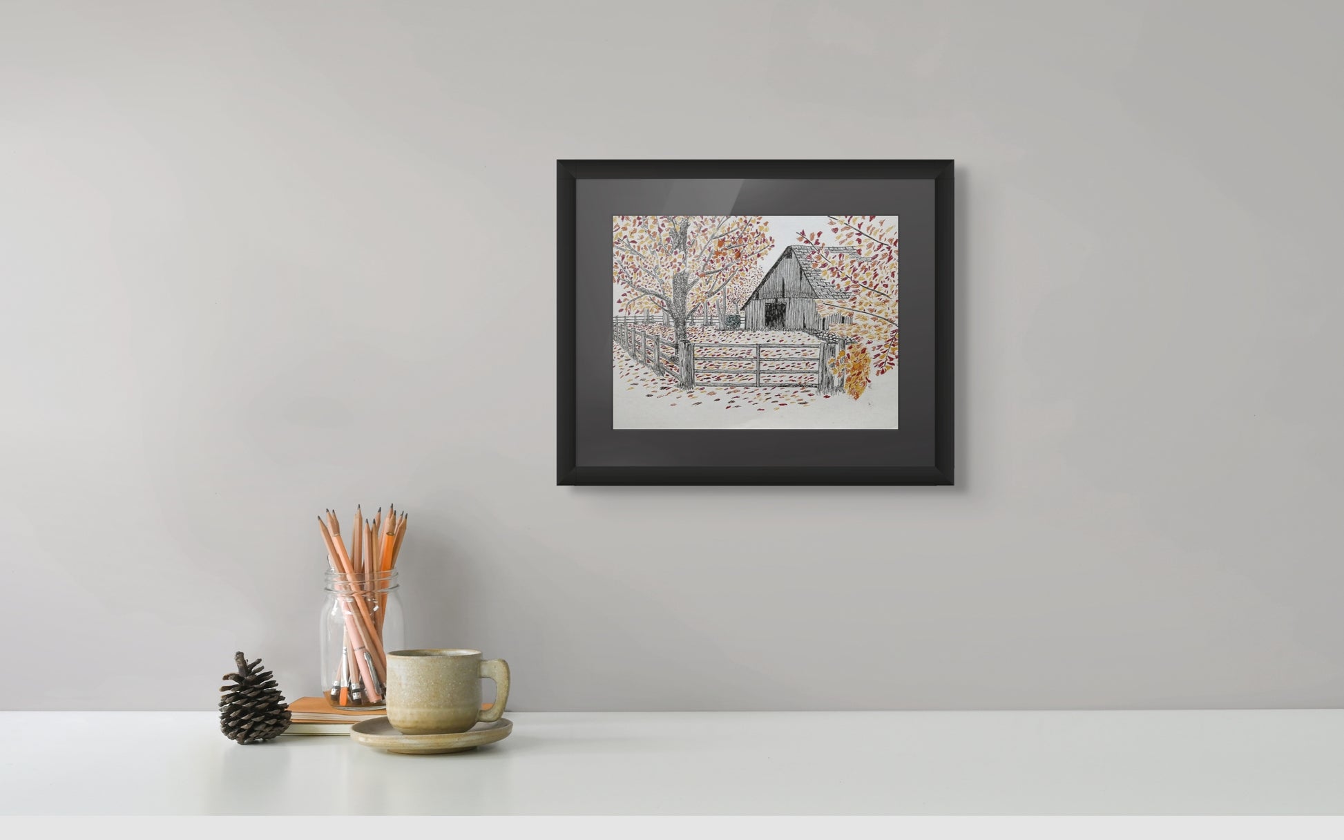Framed artwork of a rustic cabin in the woods on a white wall above a desk with stationery items.