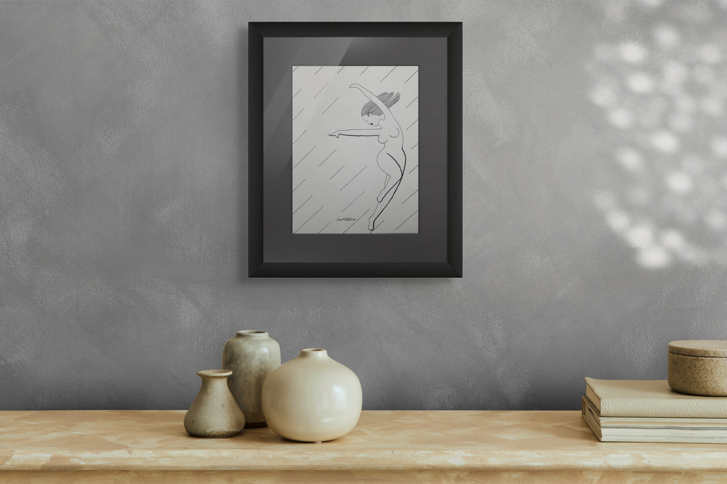 Framed artwork on a gray wall above a wooden surface with decorative items.