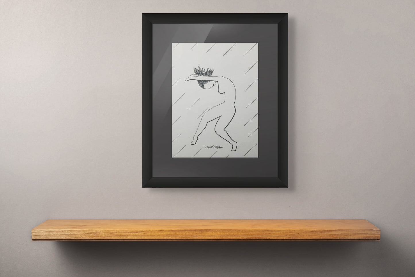 Framed artwork of a nude woman dancing above a wooden shelf against a gray wall.