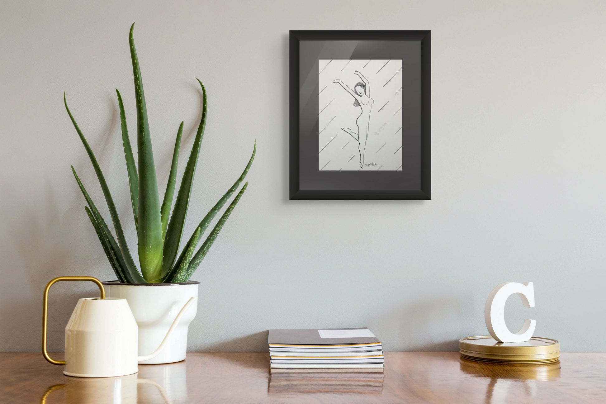Framed artwork on a wall above a table with a plant and decorative items.