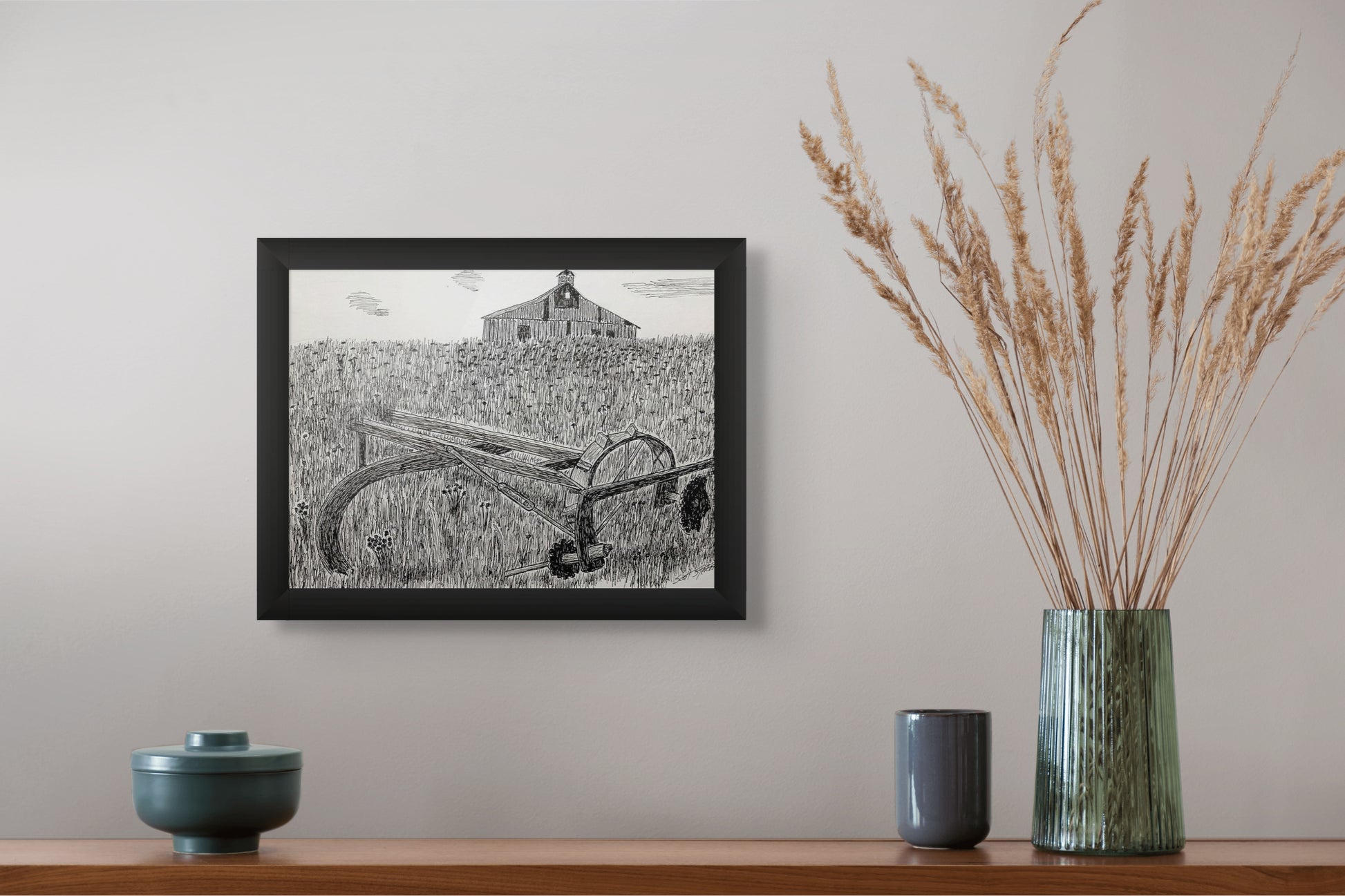 Framed black and white artwork on a wall above a wooden shelf with decorative items.