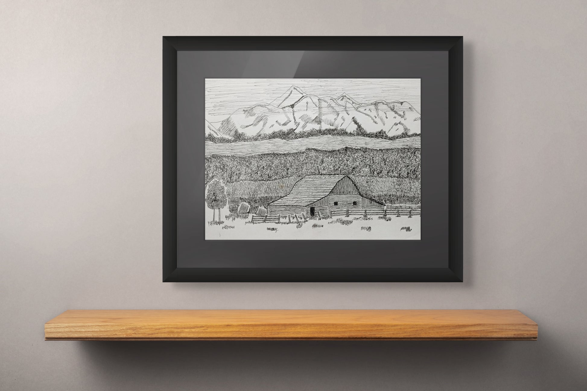 Framed black and white landscape drawing of a mountain and barn on a wooden shelf against a gray wall.