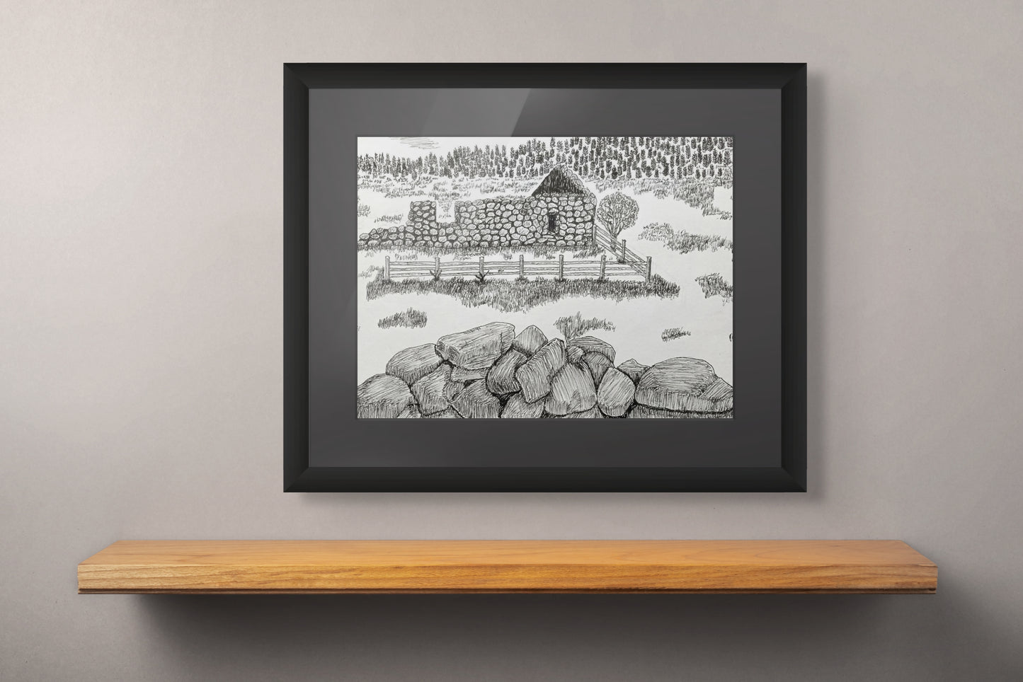 Framed black and white drawing of a stone structure on a wooden shelf against a gray wall.