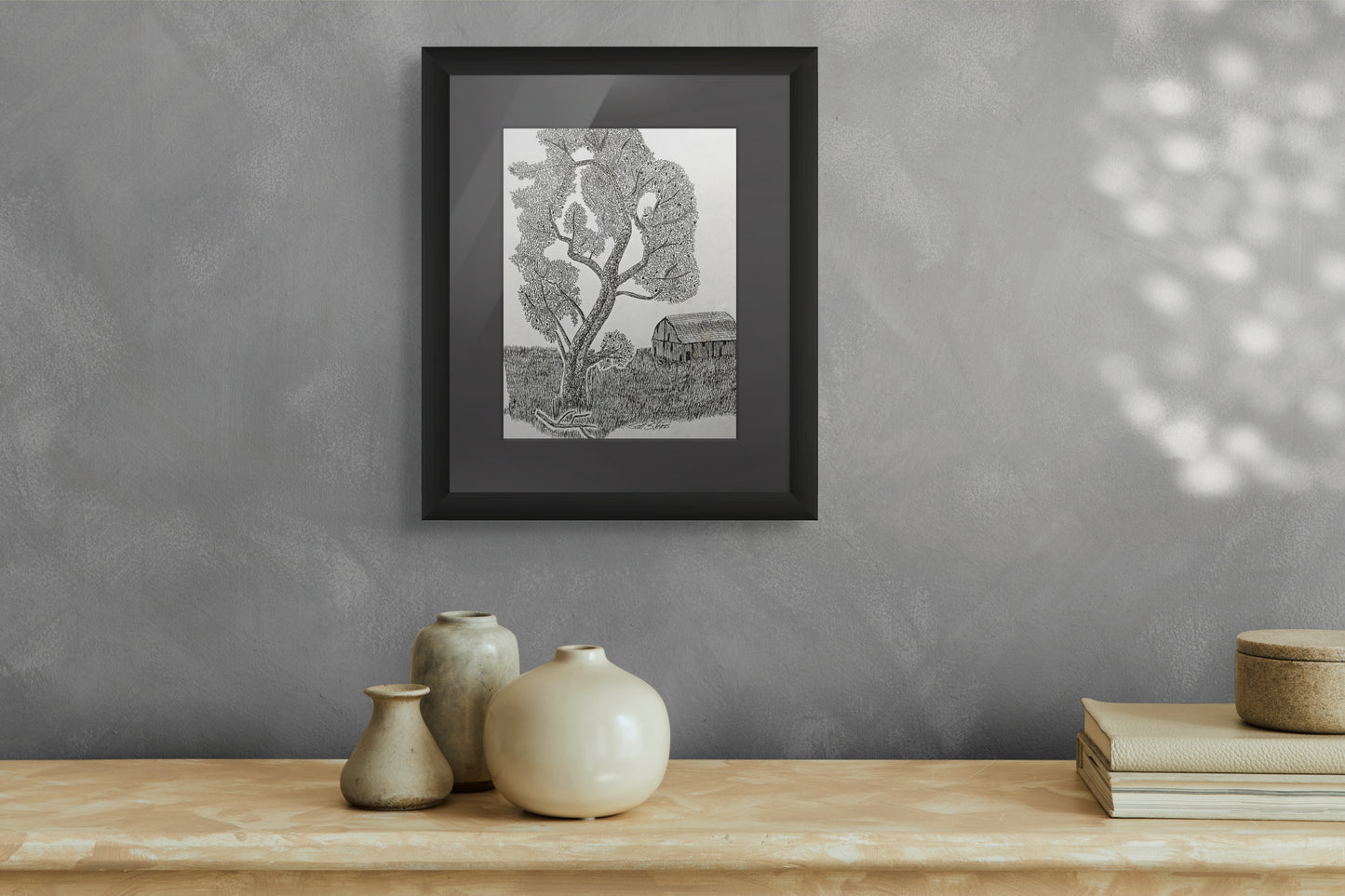 Framed black and white print of a landscape on a gray wall above a wooden shelf with decorative items.