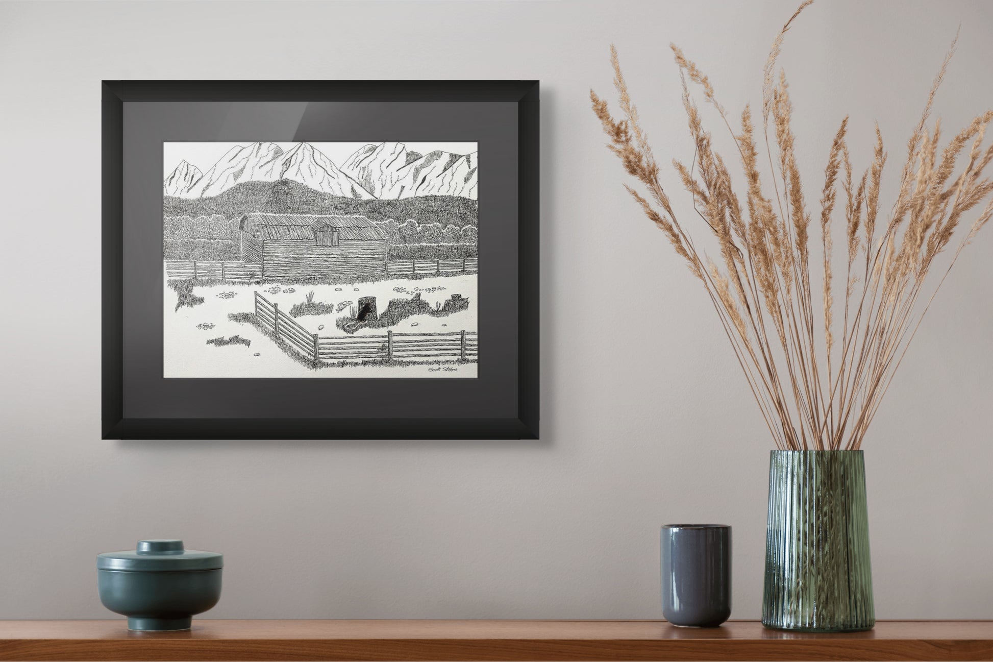 Framed black and white print on a wall above a wooden shelf with decorative items.