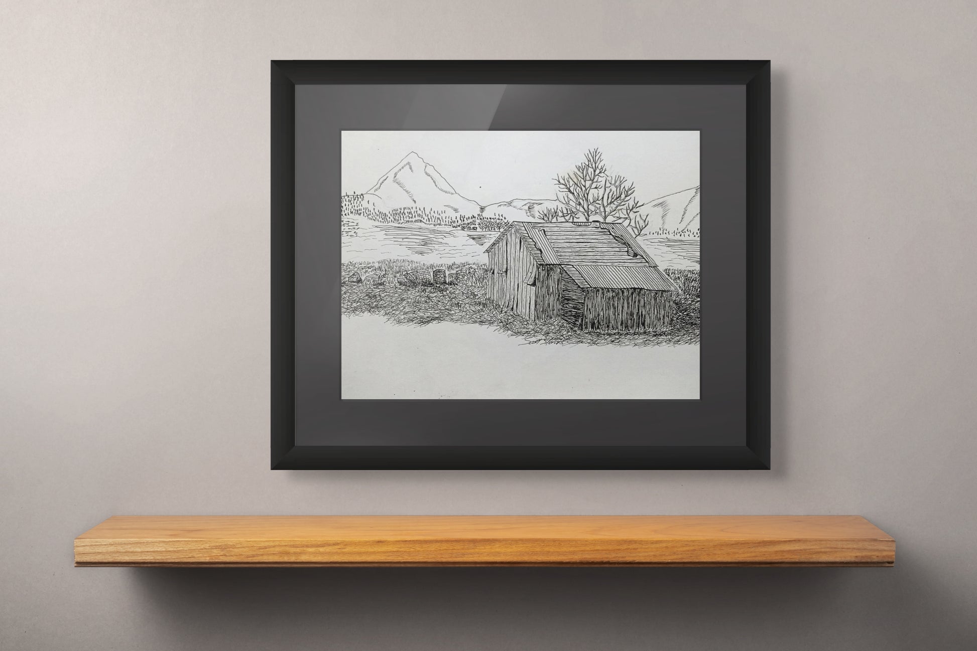 Framed black and white landscape drawing on a wooden shelf against a gray wall