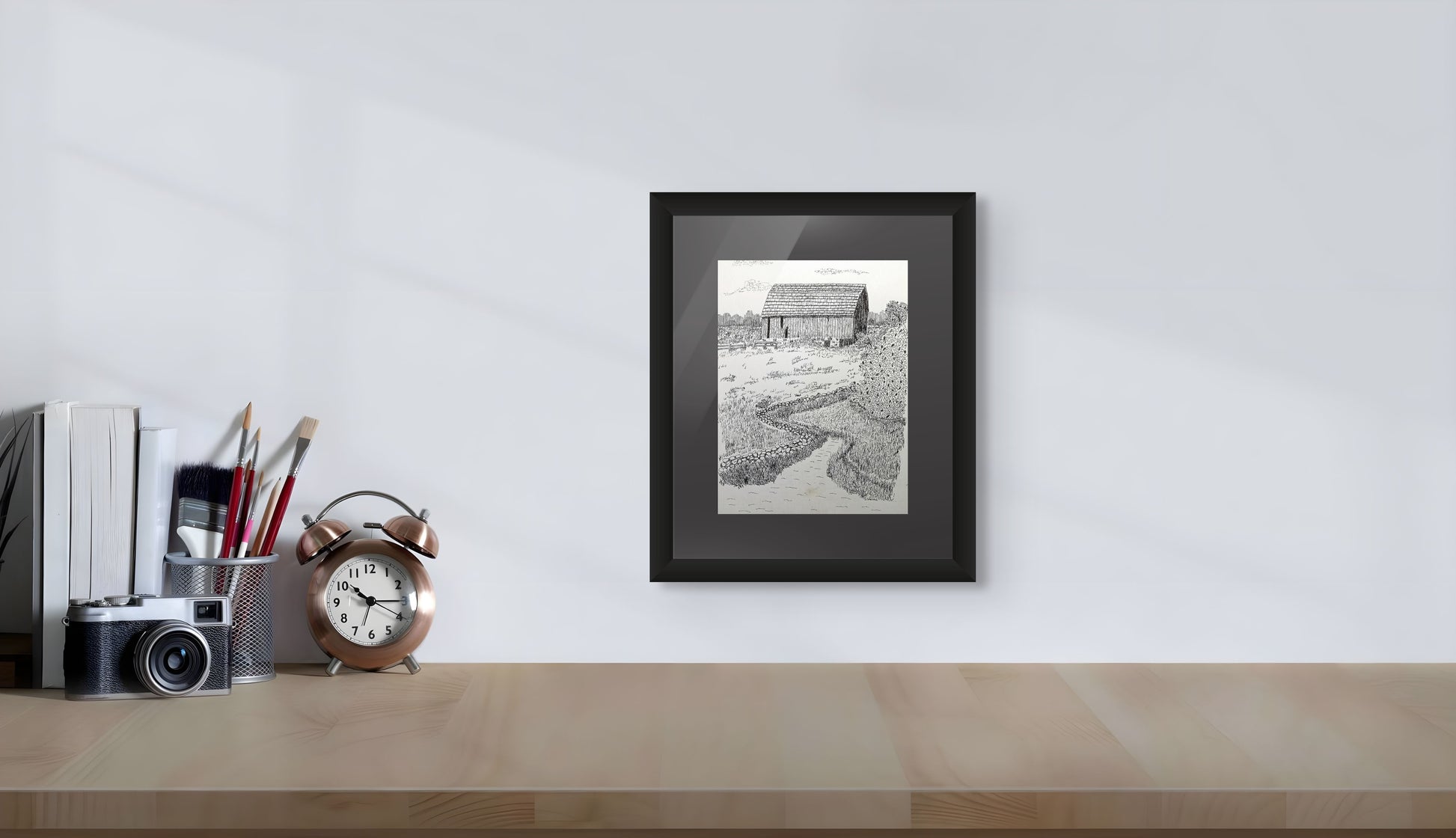 Framed black and white print of a barn and stream on a desk with office supplies
