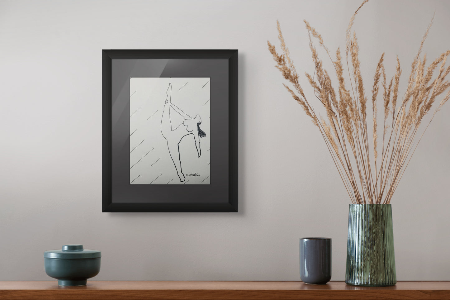 Framed artwork on a wall with decorative vases and a plant below.