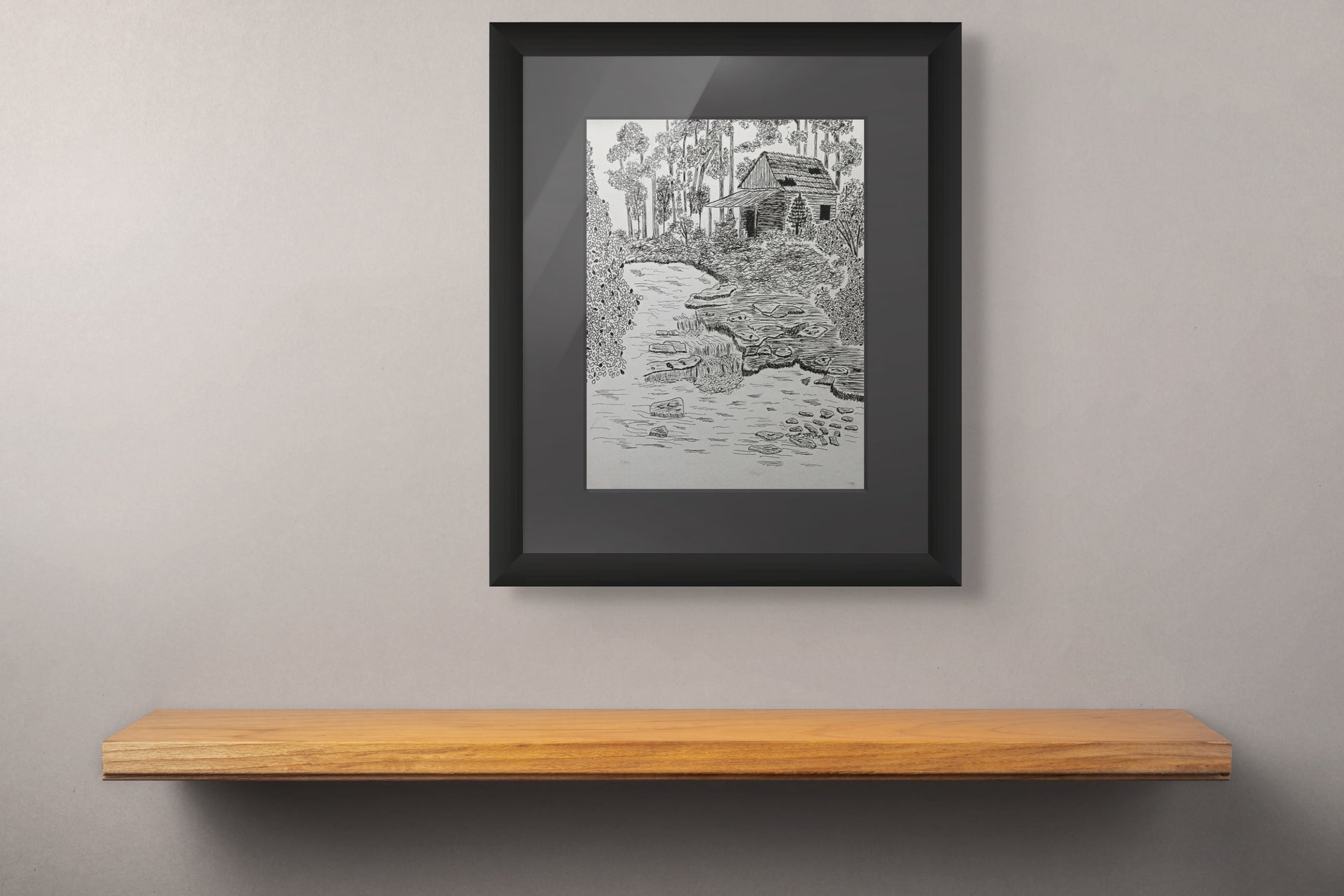 Framed pen and ink drawing of an old shack in the woods with a stream.