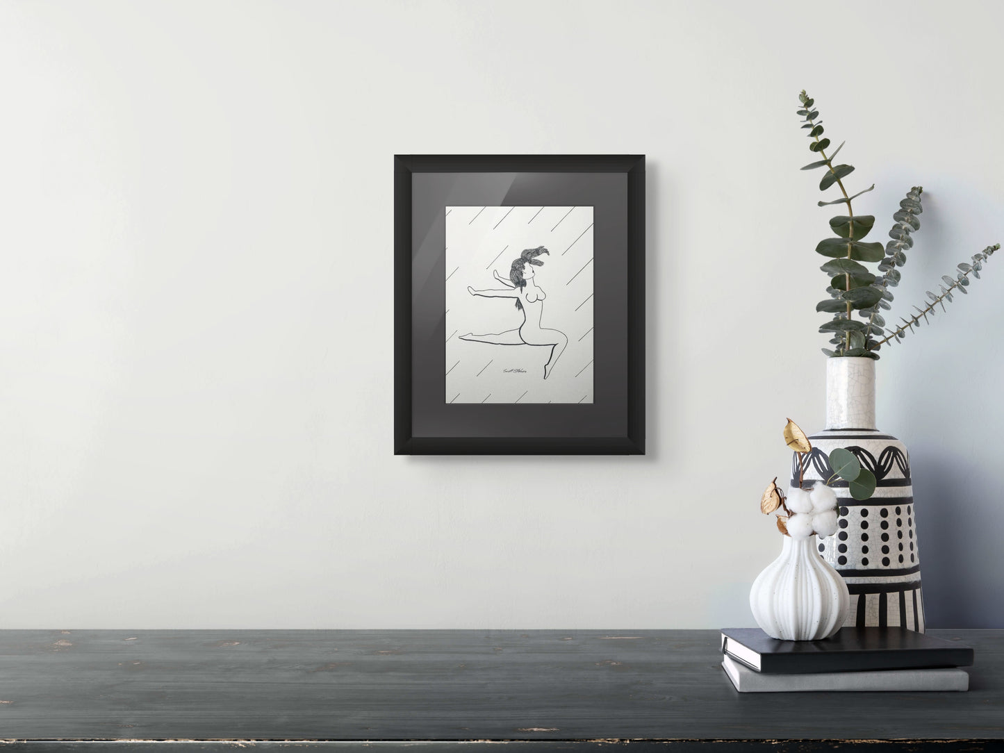 Framed artwork of a dancer on a wall above a black surface with decorative vases.