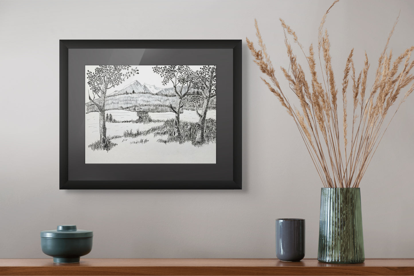 Framed black and white landscape print on a wall above a wooden shelf with decorative items.