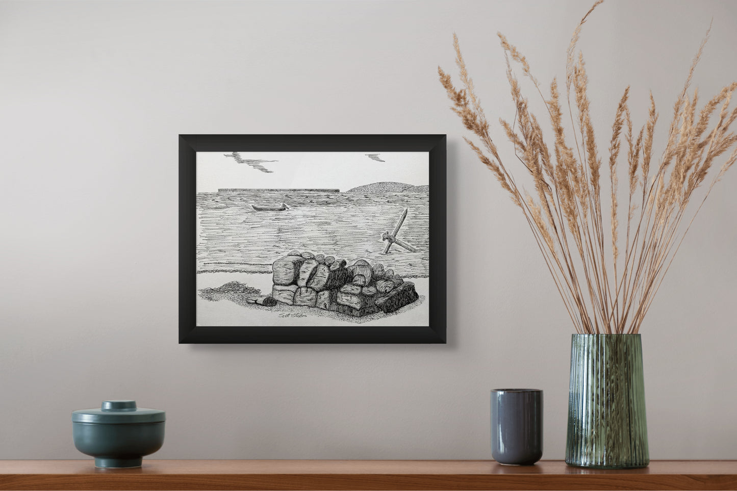 Framed black and white artwork on a wall above a wooden shelf with decorative items.