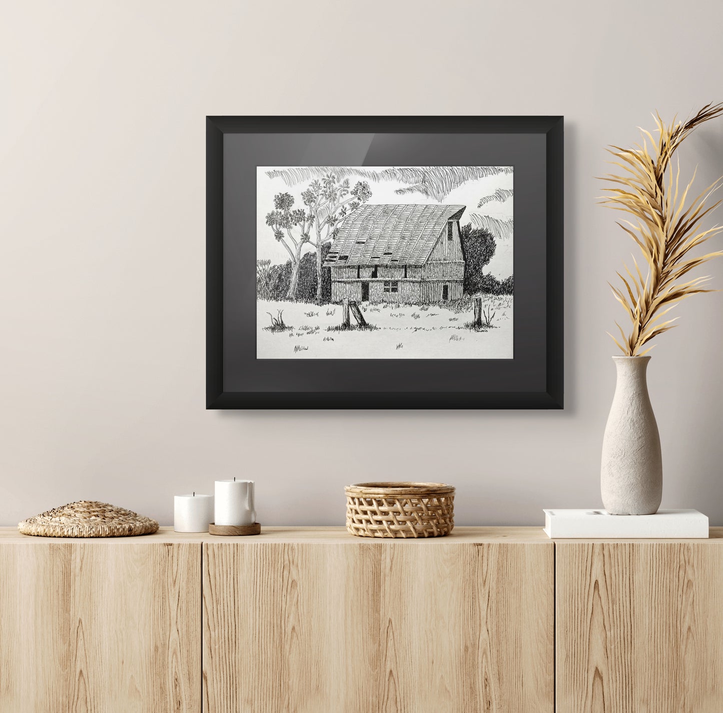 Framed black and white print of a rustic scene on a wall above a wooden cabinet.