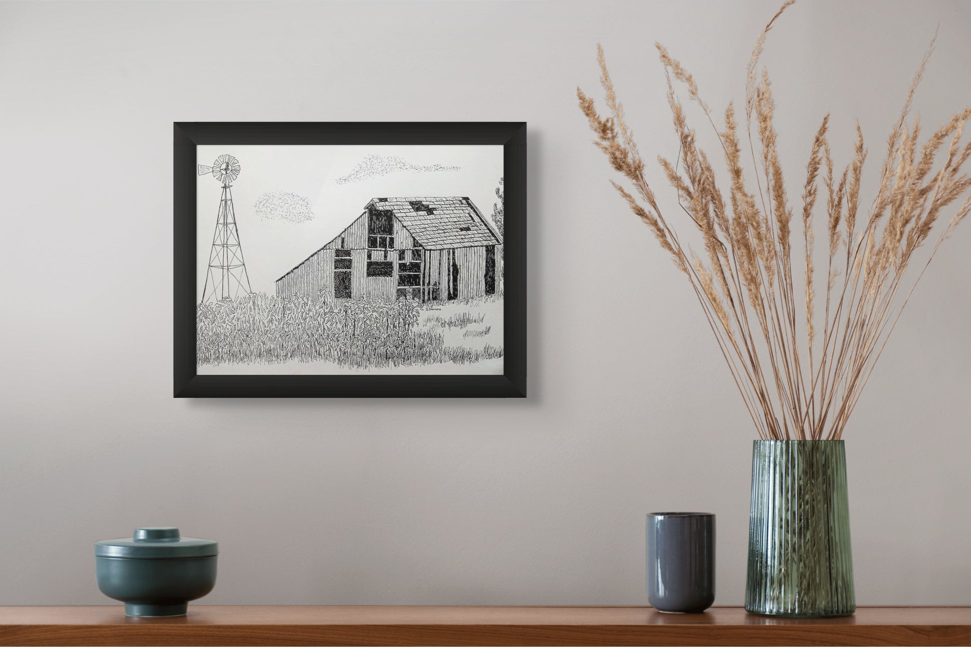 Framed black and white print of a barn with a windmill on a wall above a wooden shelf with decorative items.