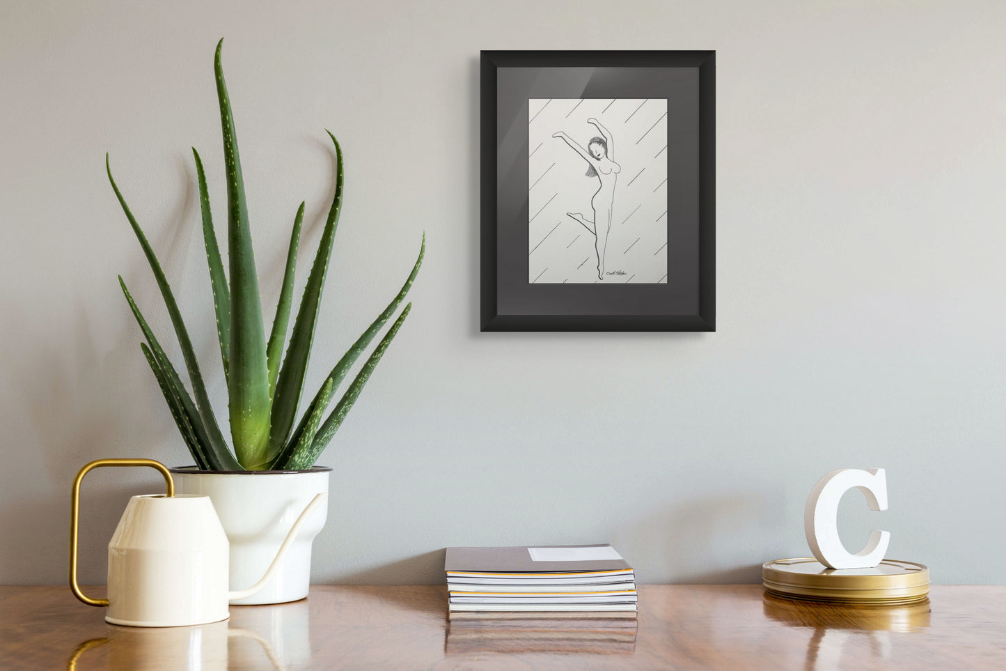 Framed artwork on a wall above a table with a plant and decorative items.