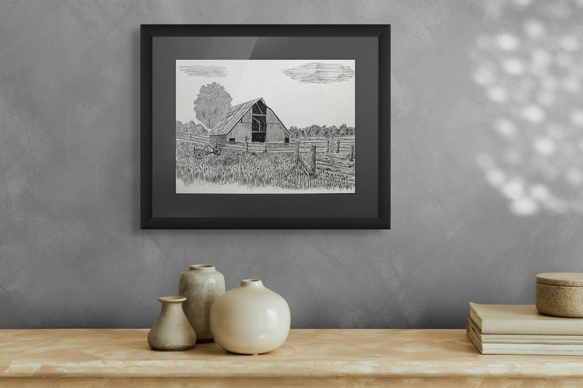 Framed black and white print of a barn on a gray wall above a wooden surface with decorative items.