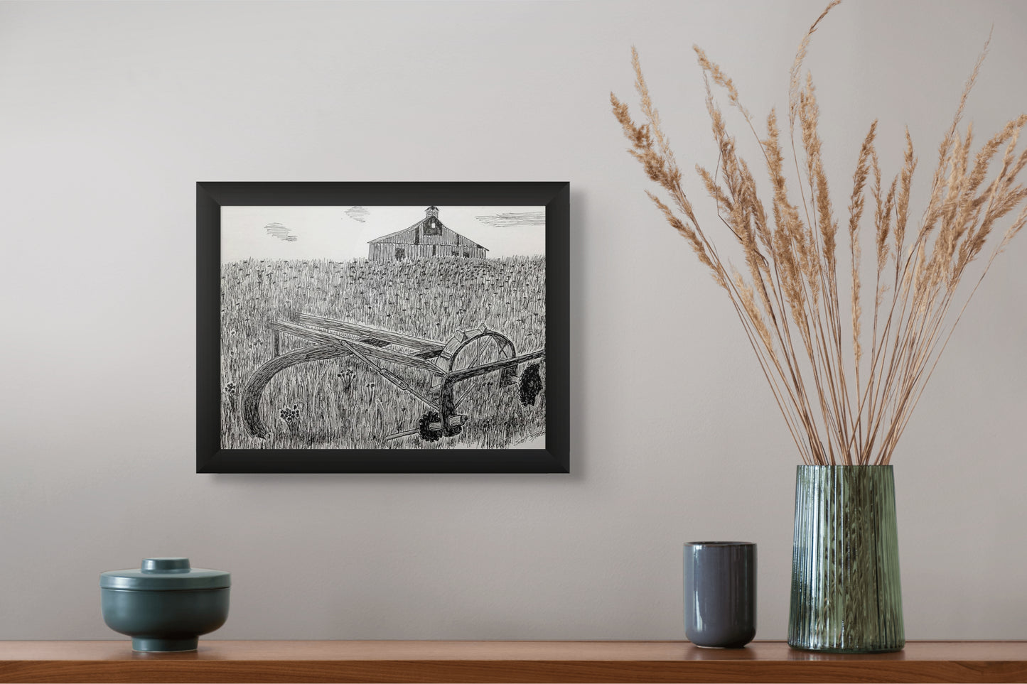Framed black and white artwork on a wall above a wooden shelf with decorative items.