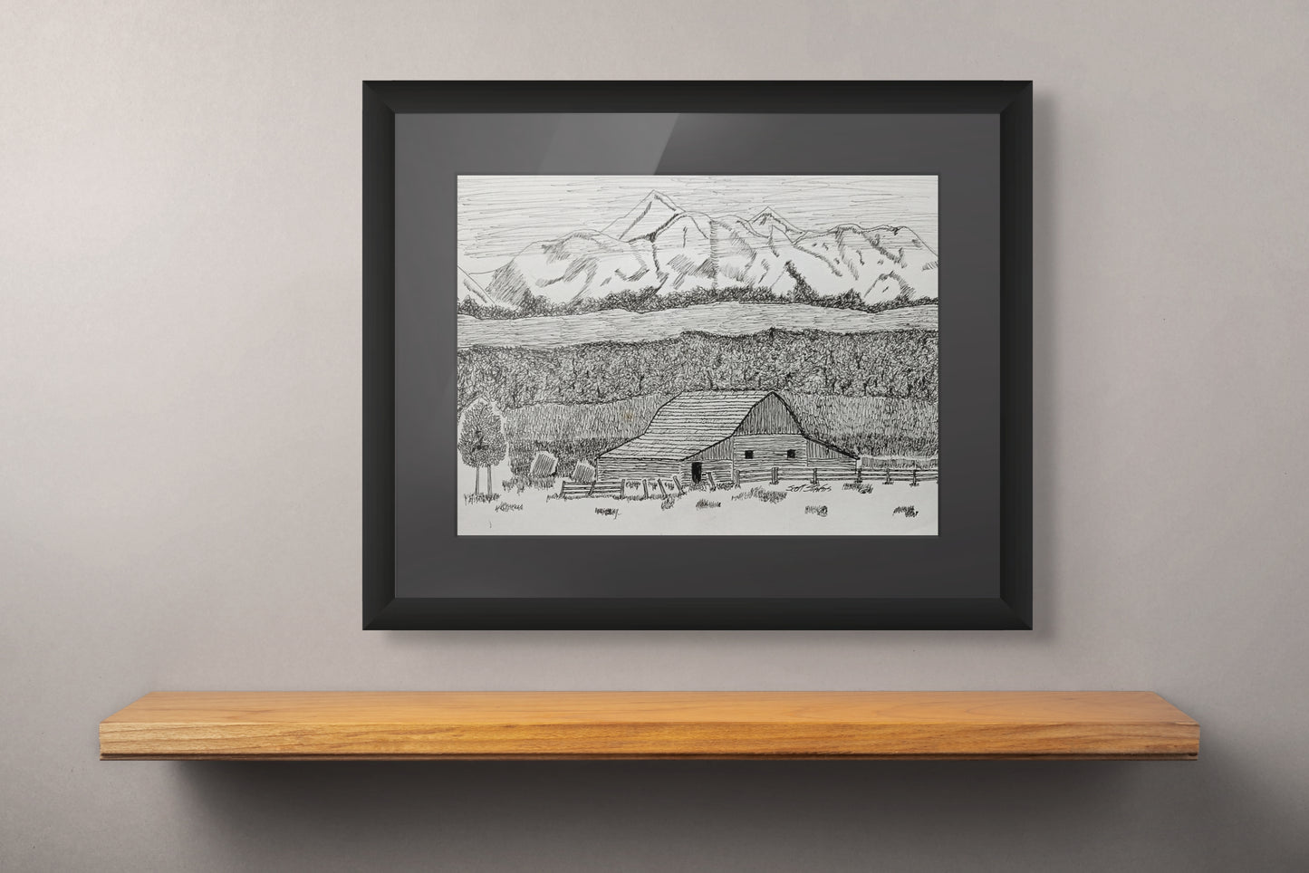 Framed black and white landscape drawing of a mountain and barn on a wooden shelf against a gray wall.