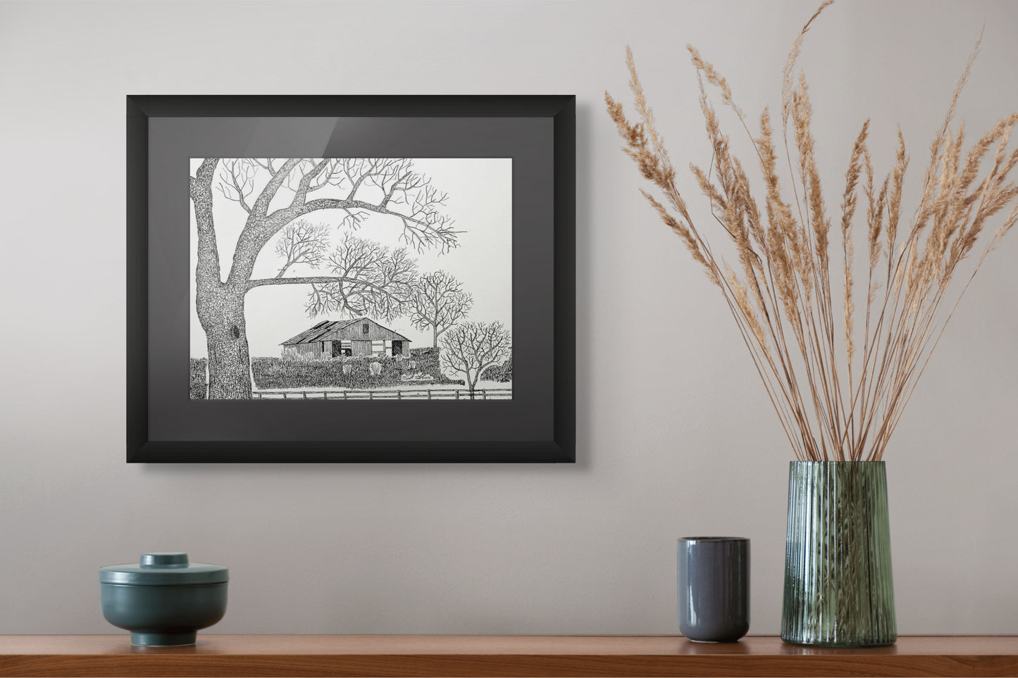 Framed black and white landscape print on a wall above a wooden shelf with decorative items.