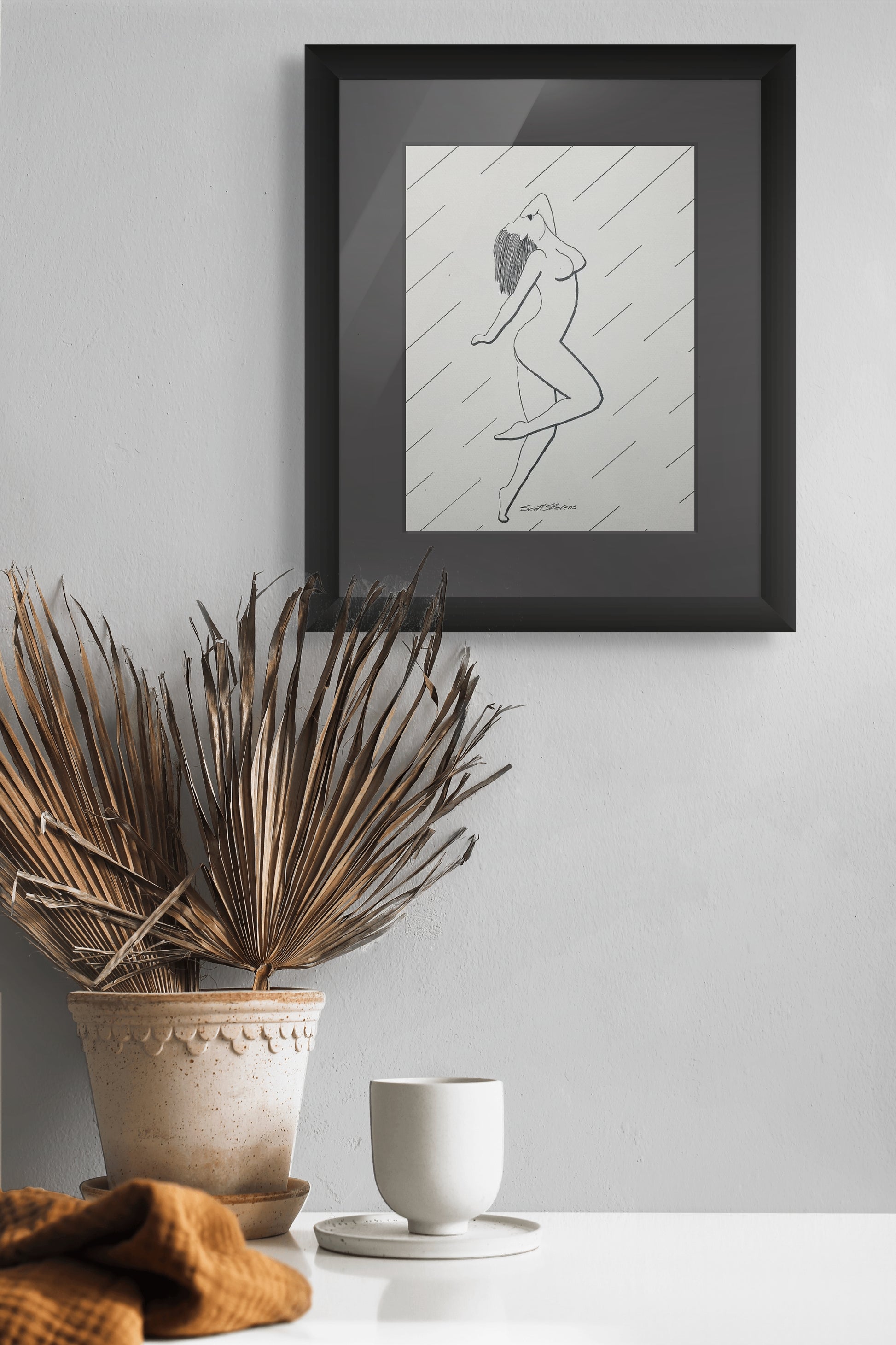 Framed black and white artwork of a dancer on a gray wall with decorative elements below.