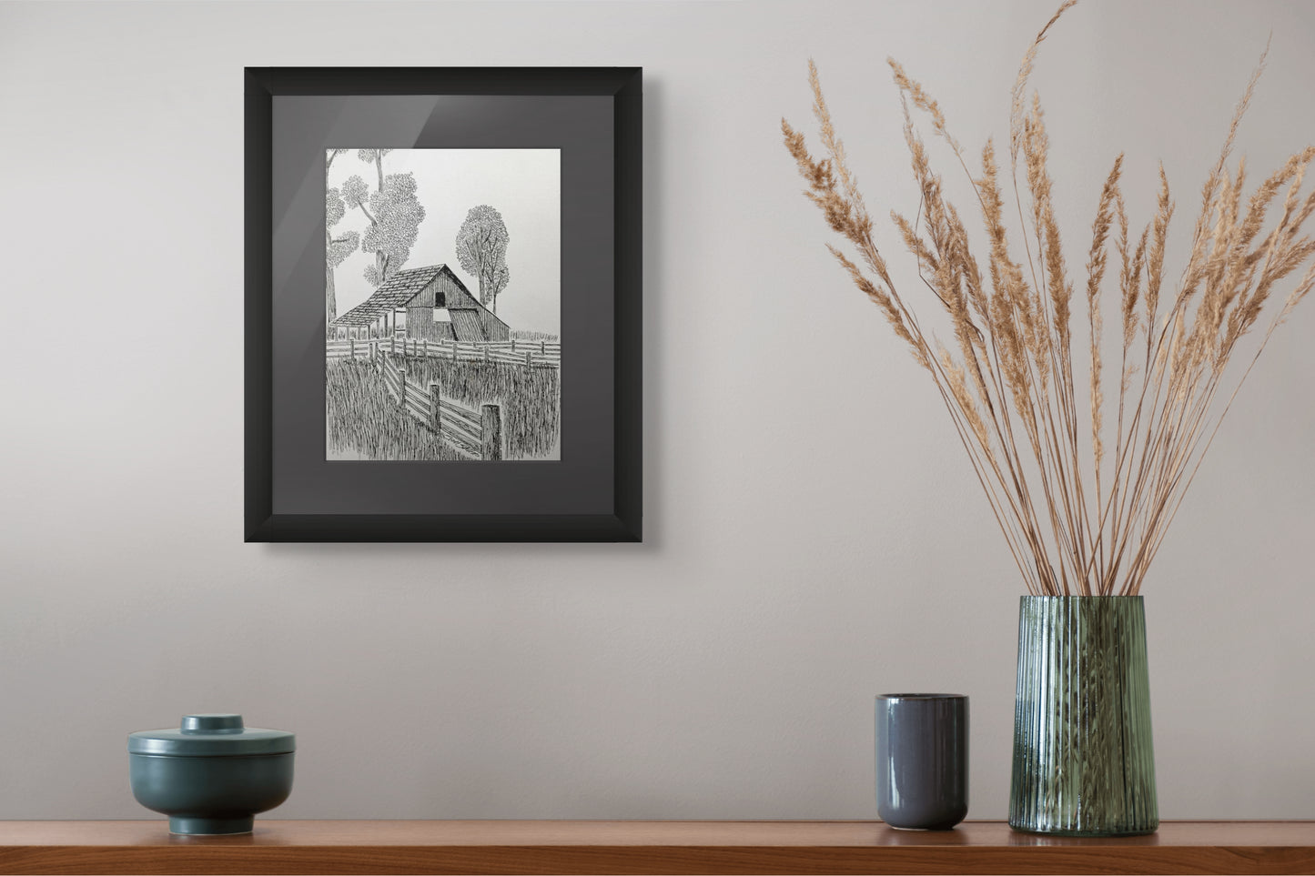 Framed black and white print of a barn on a wall above a wooden shelf with decorative items.