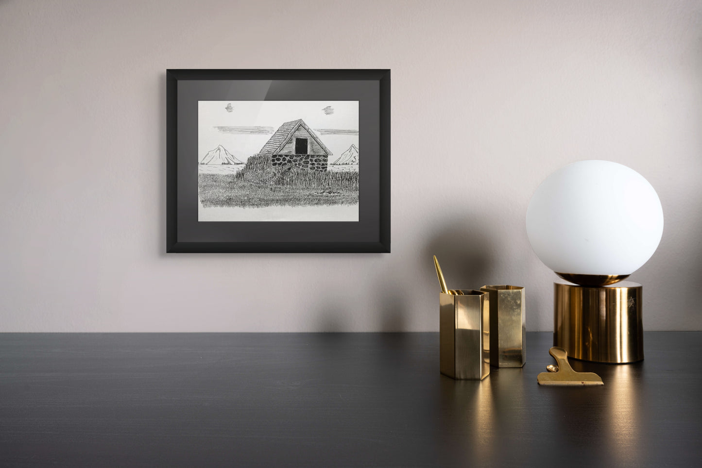 Framed black and white print of a barn on a wall above a desk with decorative items.