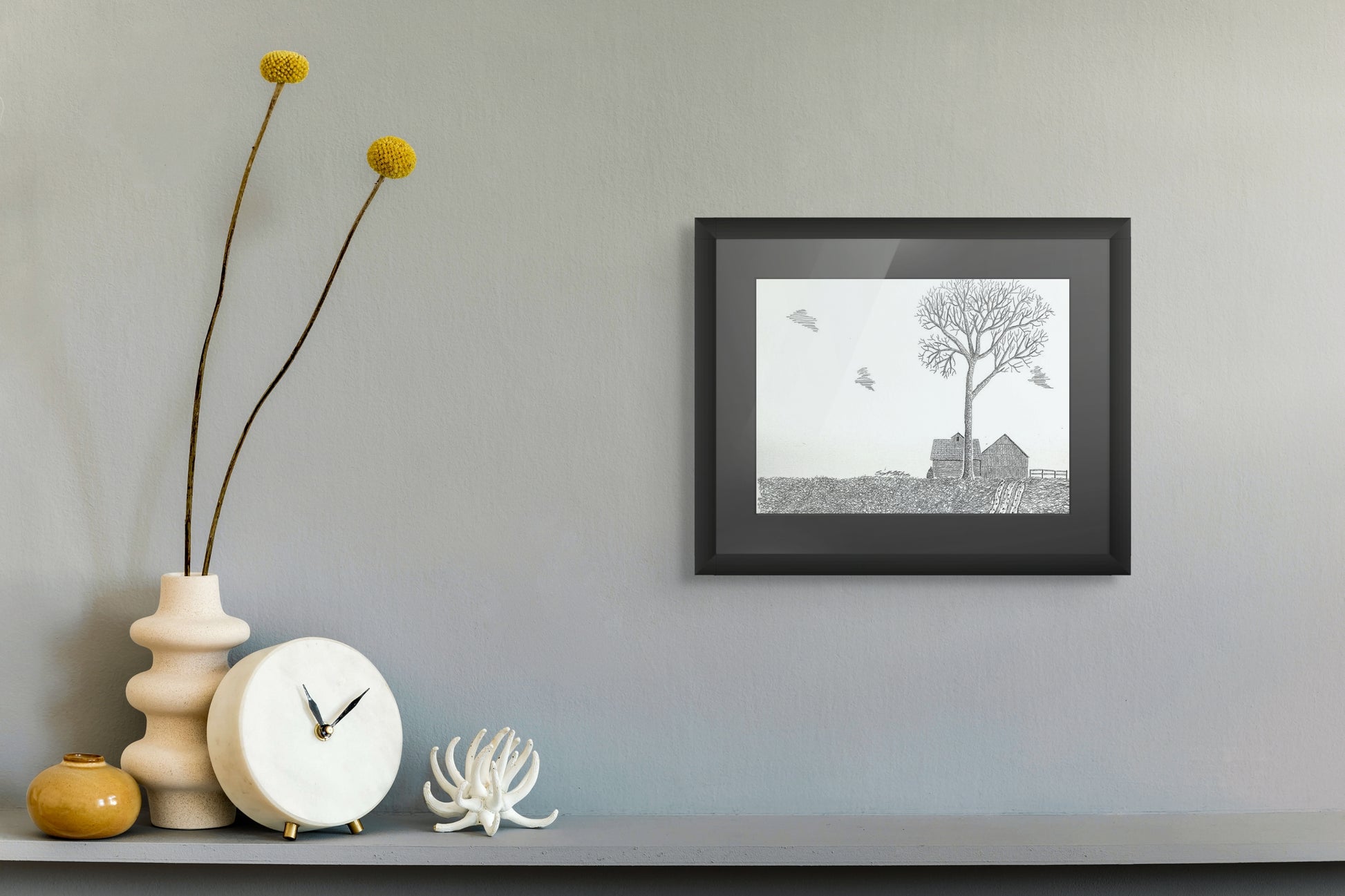 Framed black and white artwork on a wall with decorative items below.
