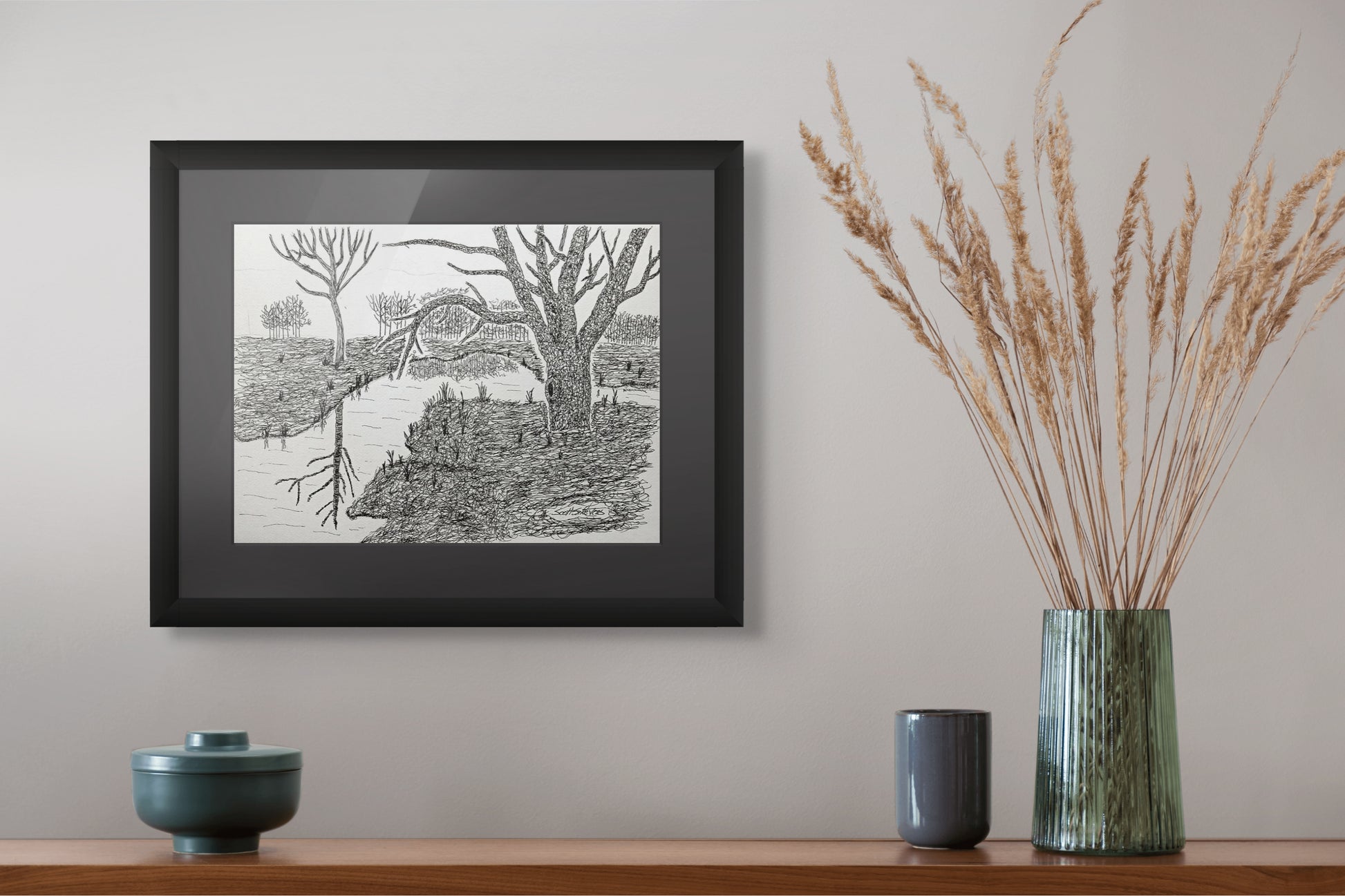 Framed black and white landscape print on a wall above a wooden shelf with decorative items.
