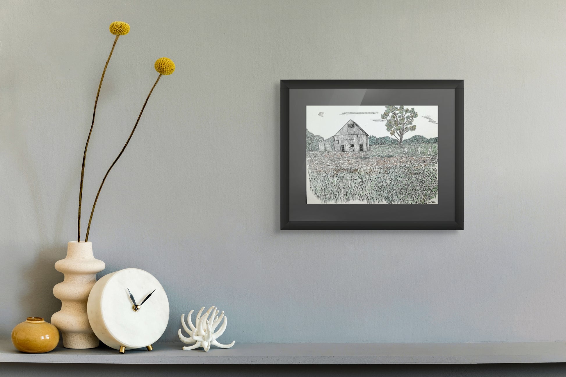 Framed artwork of a barn on a wall above a shelf with decorative items.